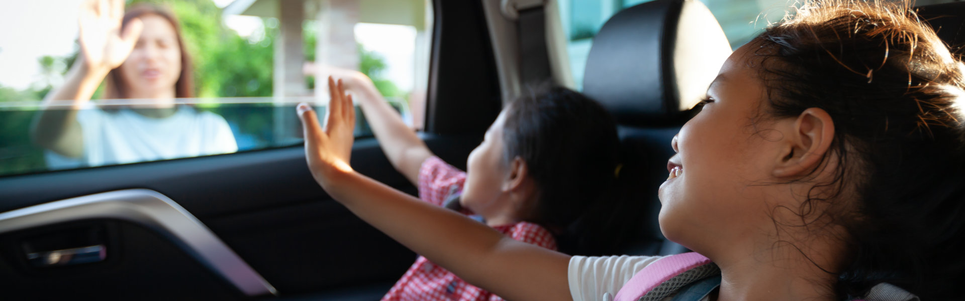 kids in the car waving goodbye to their mother